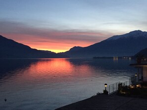 Un lac paisible au crépuscule, avec des montagnes en arrière-plan et un bâtiment illuminé sur la droite.
