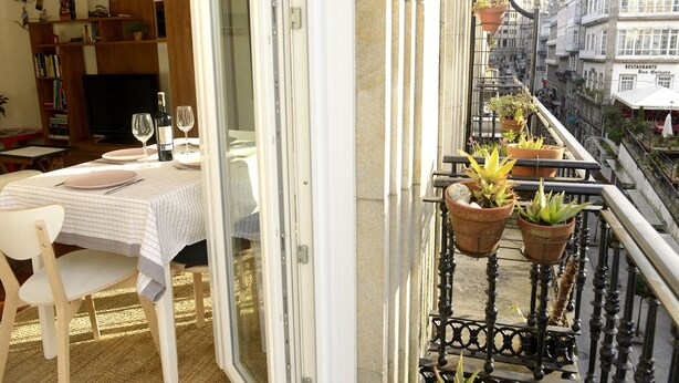 Un balcon agrémenté de plantes en pot, un coin repas avec une table dressée pour deux personnes, et une vue sur le paysage urbain.