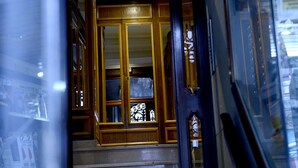 Un escalier en bois mène à une pièce dotée d’une grande fenêtre et d’une porte avec une poignée.