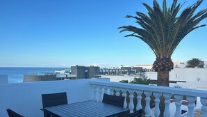 A terrace with a table and chairs, a palm tree, and a view of the sea and buildings. - Front line, contemporary,  refurbished, stunning sea views, pool, WiFi, SKY (Puerto del carmen)