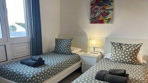A hotel room with two beds, each with patterned bedding and pillows, a bedside table with a lamp, and a colorful abstract painting on the wall. - Front line, contemporary,  refurbished, stunning sea views, pool, WiFi, SKY (Puerto del carmen)