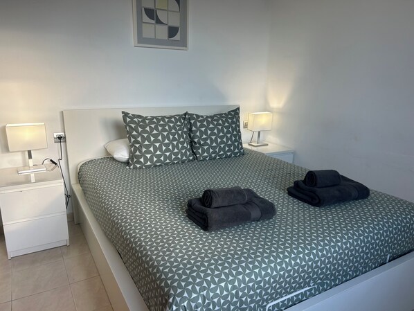 A neatly made bed with patterned bedding, two bedside lamps, a wall art piece, and a folded towel on the bed. - Front line, contemporary,  refurbished, stunning sea views, pool, WiFi, SKY (Puerto del carmen)
