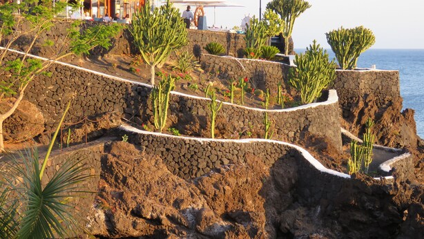 A rocky coastal area with a stone pathway leading to a restaurant with outdoor seating. - Front line, contemporary,  refurbished, stunning sea views, pool, WiFi, SKY (Puerto del carmen)