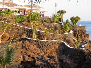 A rocky coastal area with a stone pathway leading to a restaurant with outdoor seating. - Front line, contemporary, refurbished, stunning sea views, pool, WiFi, SKY (Puerto del carmen)