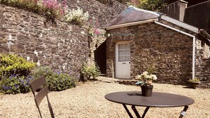 A stone building with a door, a small garden with flowers, and a table with a chair. - Beautiful Historic Grade II Listed Georgian Town House (Llandeilo)
