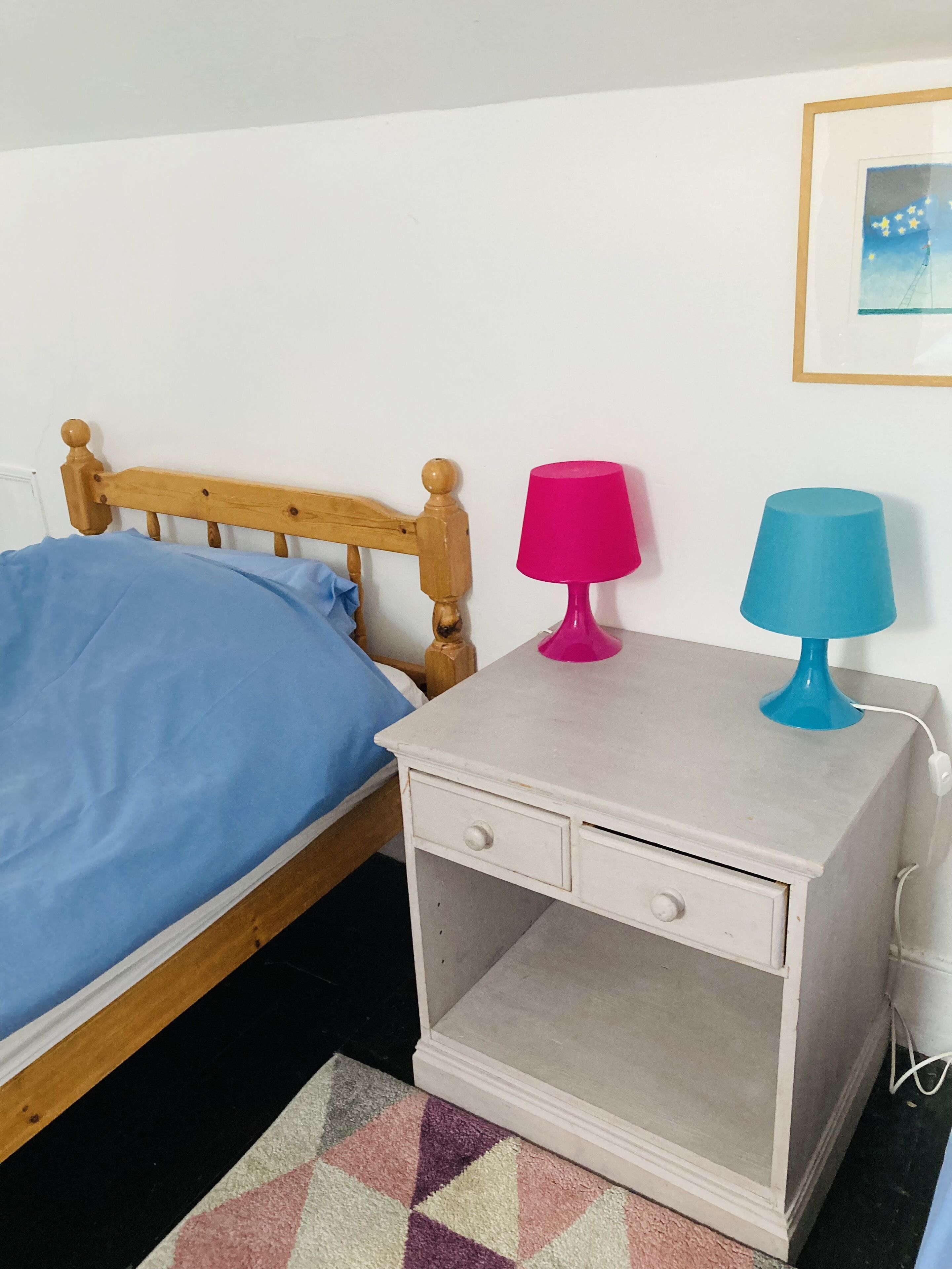 Ein Schlafzimmer mit einem hölzernen Bett, einem Nachttisch mit zwei Lampen und einem gerahmten Bild an der Wand.