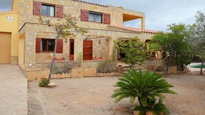 A stone building with a yellow facade, multiple windows with wooden shutters, and a small garden area with a palm tree. - Beautiful private villa for 8 people with private pool, TV, patio, pets allowed and panoramic view (L'ampolla)