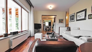 Sala de estar con sofá, una mesa de centro y televisor. Se ve una ventana con cortinas, un radiador y una planta.