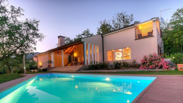 Una casa moderna con piscina, un porche cubierto y un jardín bien cuidado.