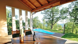 Un área de comedor al aire libre techada con una piscina al fondo.