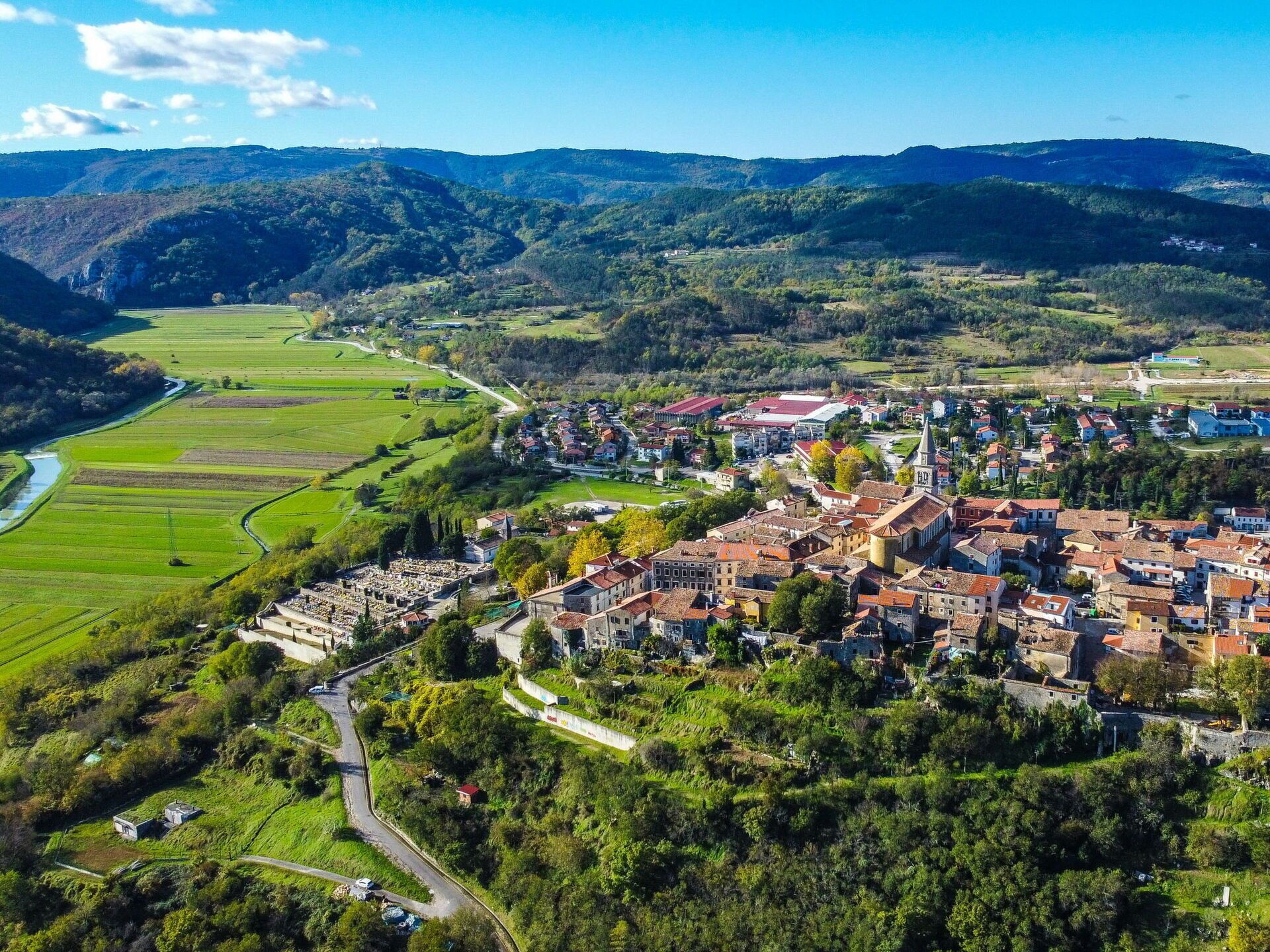 Un pueblo con un río, campos verdes y una combinación de edificios tradicionales y modernos.