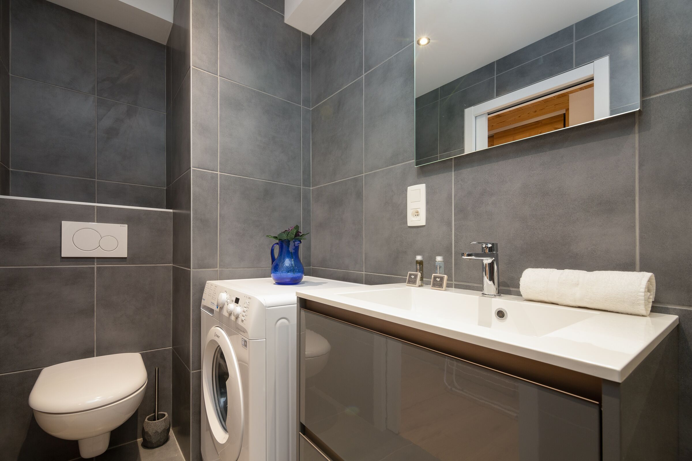 A modern bathroom with a washing machine, a sink, and a toilet.