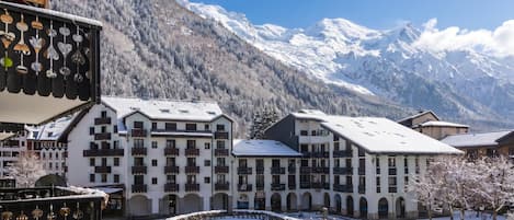 Un patio cubierto de nieve con edificios, un paisaje de montañas al fondo y cielo despejado.