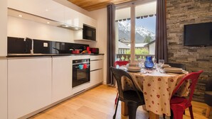 Een moderne keuken met een eethoek, houten plafond, stenen muur en een aan de muur bevestigde televisie.