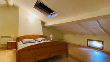 A bedroom with a wooden bed, a nightstand, a lamp, a small window, and an attic space with a skylight.