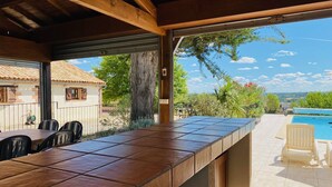 Un patio exterior con barra de baldosas, piscina y vistas al paisaje circundante.