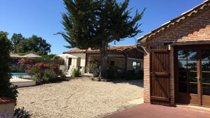 Una propiedad residencial con camino de grava, un gran árbol de coníferas y un edificio de ladrillo con puerta de madera.