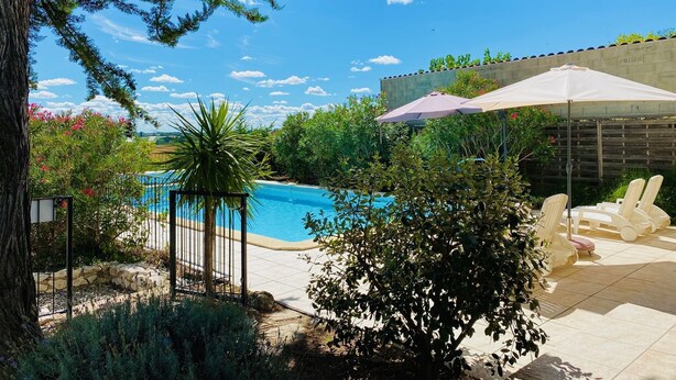 Patio trasero con piscina, rodeado de follaje y una pérgola con sombrillas.