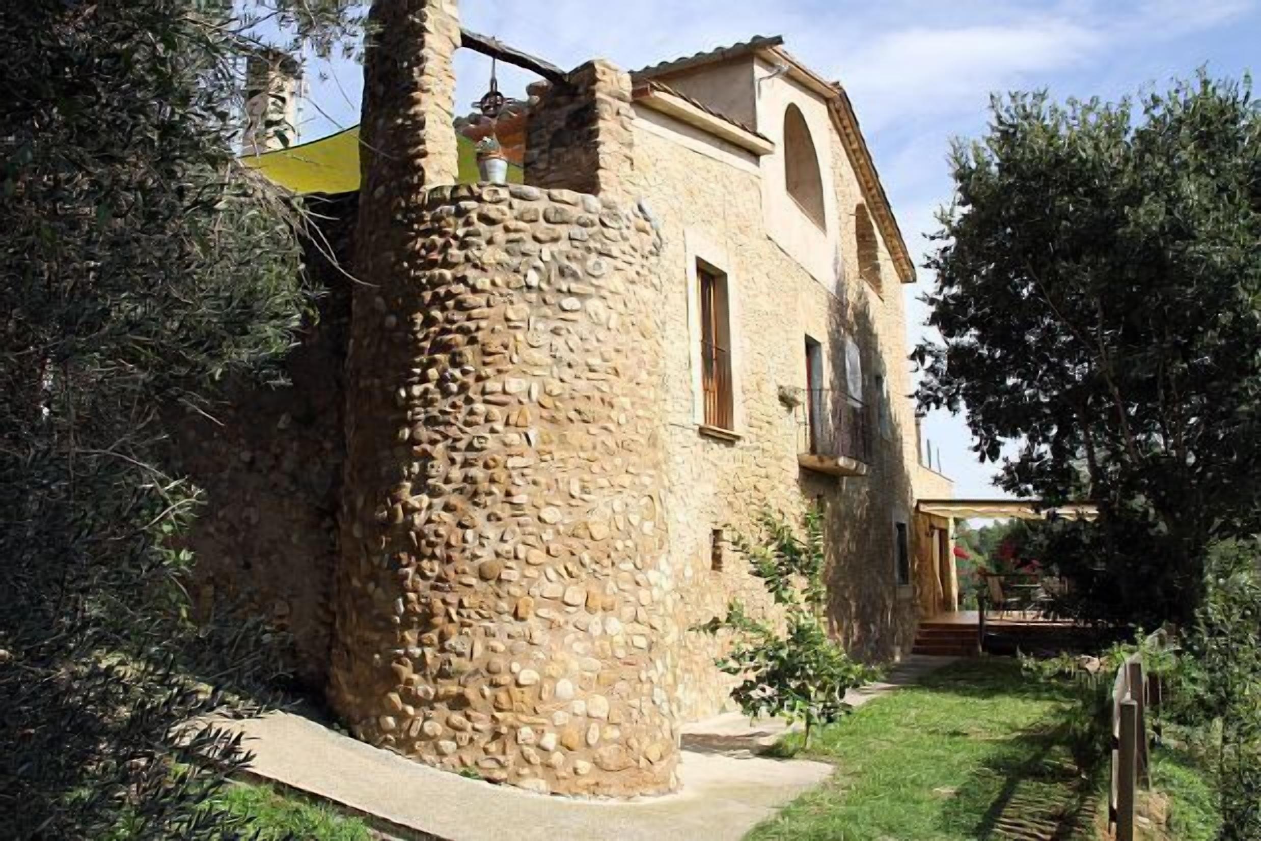 A stone tower attached to a building with a balcony, surrounded by greenery.
