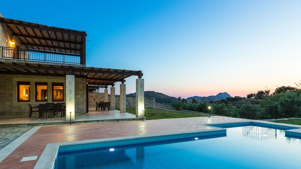 A poolside area with a stone building, outdoor seating, and a view of the mountains.