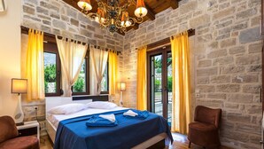 A bedroom with a stone wall, a bed with blue bedding, yellow curtains, and a wooden floor.