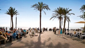 Un área de comedor al aire libre con mesas y sillas, palmeras y vistas a la playa.