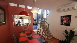 Un área de comedor con una mesa a cuadros roja y negra, un espejo y una escalera con barandillas verdes que conduce a una zona de cocina.