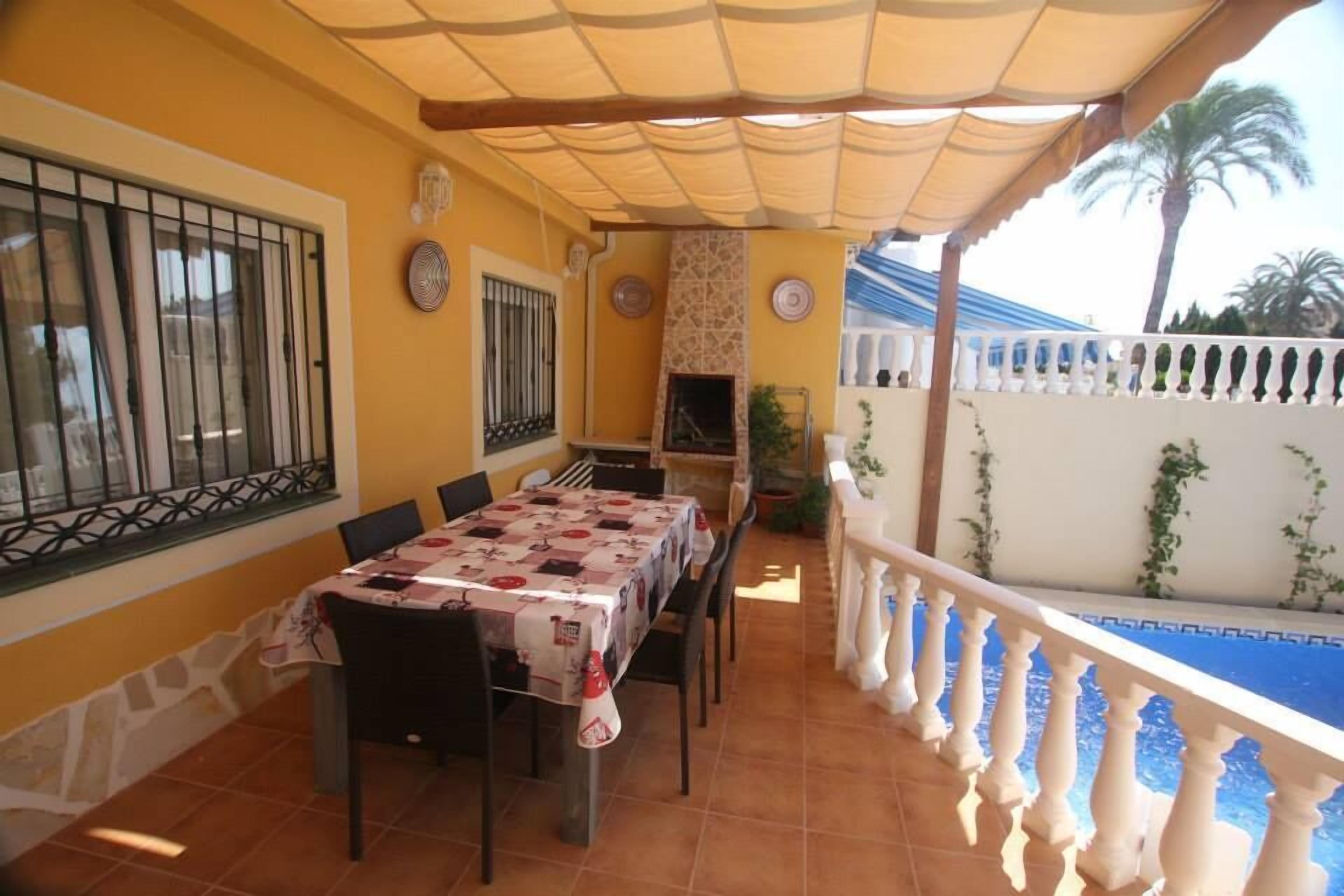 Un patio couvert avec une table et des chaises, une cheminée et une vue sur une piscine.