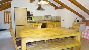 Een gezellig keuken in zolderstijl met houten balken, een houten eettafel en eenvoudige apparaten.