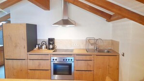Een kleine keuken met houten kastjes, een roestvrijstalen fornuis, een koffiezetapparaat en een spoelbak.