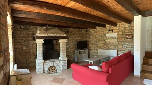 A stone fireplace with a television, a red sofa, and a wooden ceiling.
