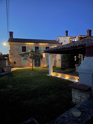 A stone house with a tiled roof, a small garden, and outdoor lighting.