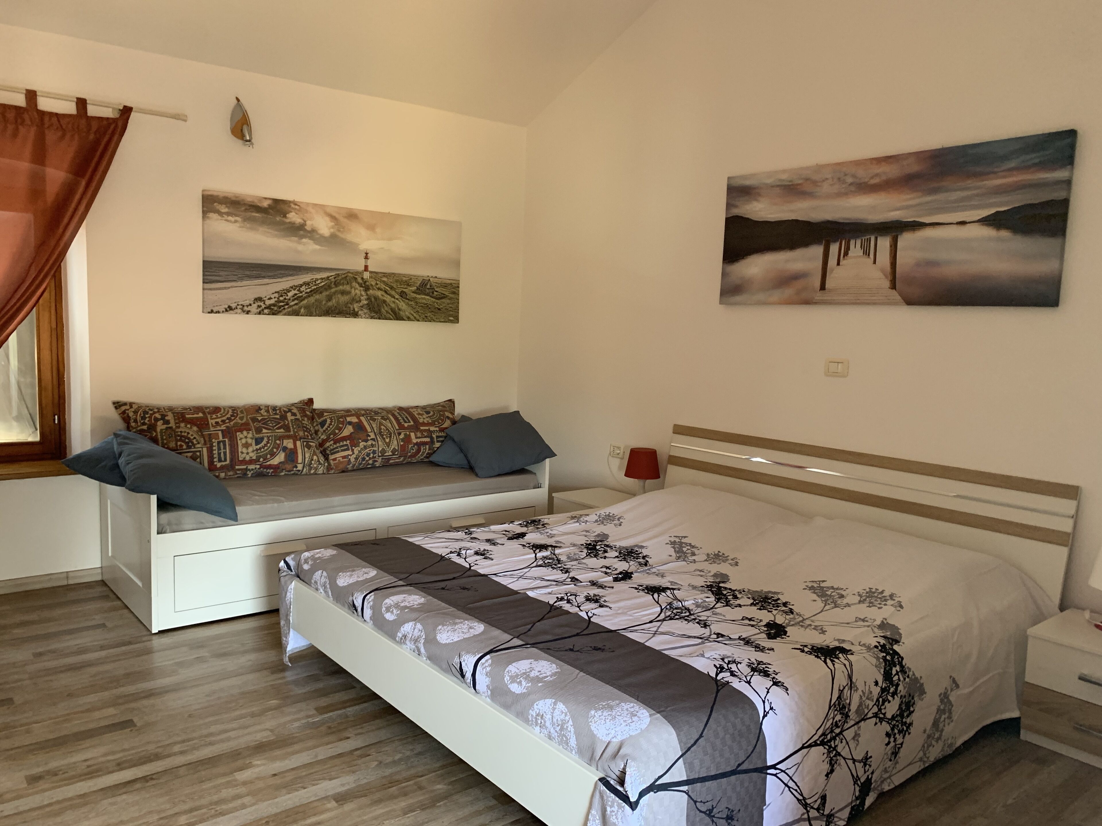 Et soveværelse med seng, sovesofa, et natbord, en lampe og to billeder på væggen.