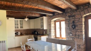 A rustic kitchen with white cabinets, a wooden ceiling, and a stone wall.