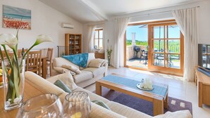 A living room with a sofa, coffee table, and a dining area with chairs. There's a bookshelf and a TV. - Nice apartment in villa for 6 guests with WIFI, pool, A/C, TV and terrace (Umag)