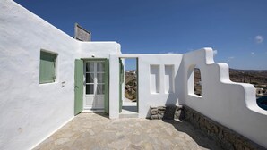 A white building with a stone-tiled entrance, a green door, and a small window.