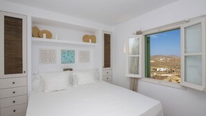 A bedroom with a large bed, a window with a view of a landscape, and decorative wall art.