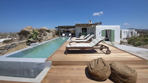 A poolside area with lounge chairs, a wooden deck, and a view of the surrounding landscape.