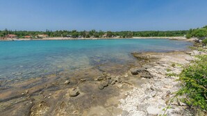 A coastal area with clear turquoise water, rocky shore, and buildings in the background. - Stunning  villa for 6 people with private pool, WIFI, A/C, TV, terrace and pets allowed (Umag)