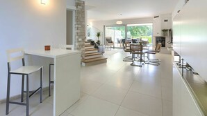 A modern kitchen with white cabinetry, a dining area with a glass table, and a staircase leading to a balcony. - Stunning  villa for 6 people with private pool, WIFI, A/C, TV, terrace and pets allowed (Umag)