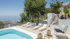 A poolside area with lounge chairs, a small table, and a view of the sea. - SODA Y LIMÓN - Amazing sea and mountain views, private (heated) pool, air conditioning (Sayalonga)
