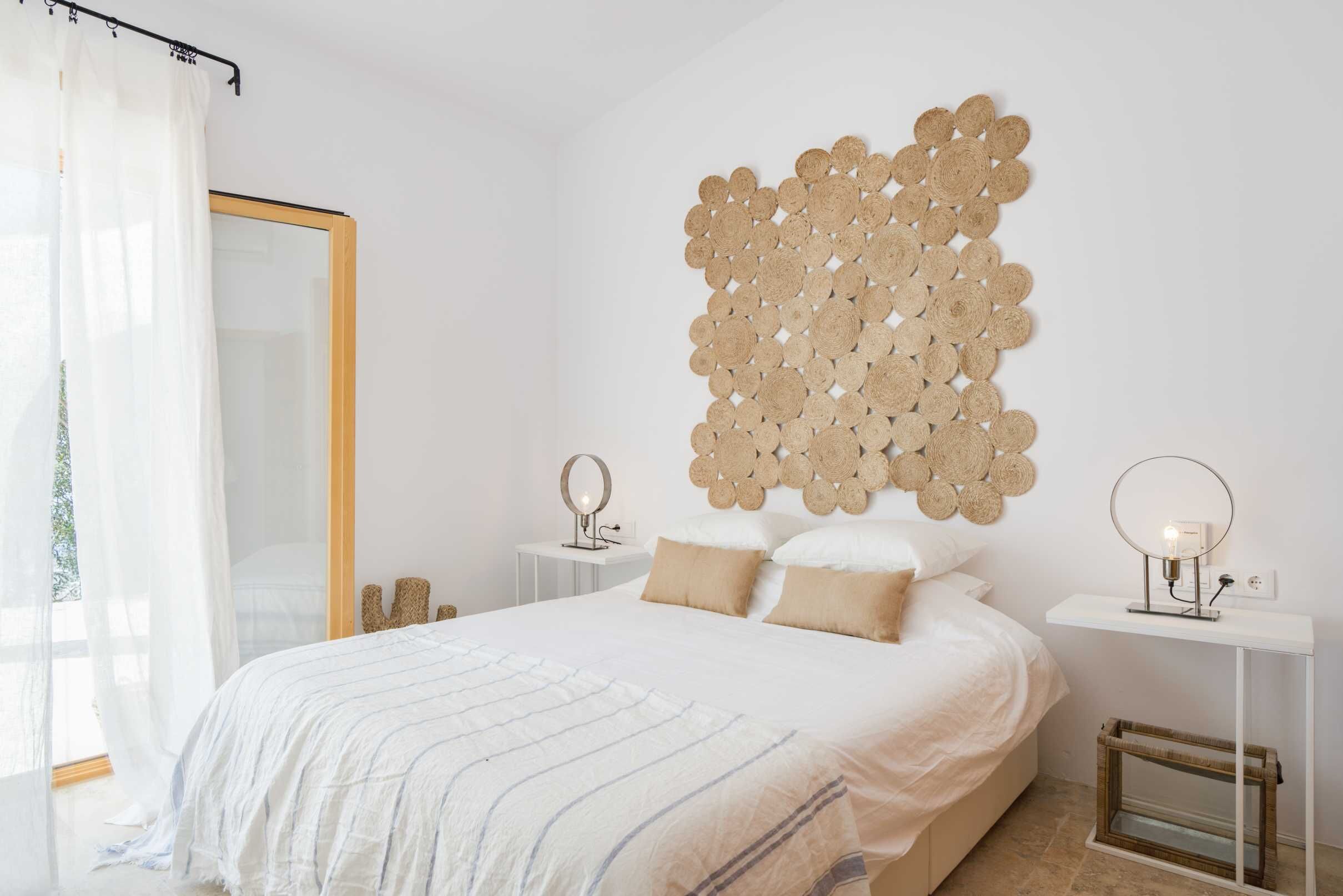 A bedroom with a bed, bedside tables, a mirror, and a wall art piece.