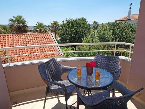 A balcony with a round table and two chairs, a vase with a red rose, and two glasses of orange juice. - Beautiful apartment for 4 guests with A/C, WIFI, pool, TV and terrace (Zadar)
