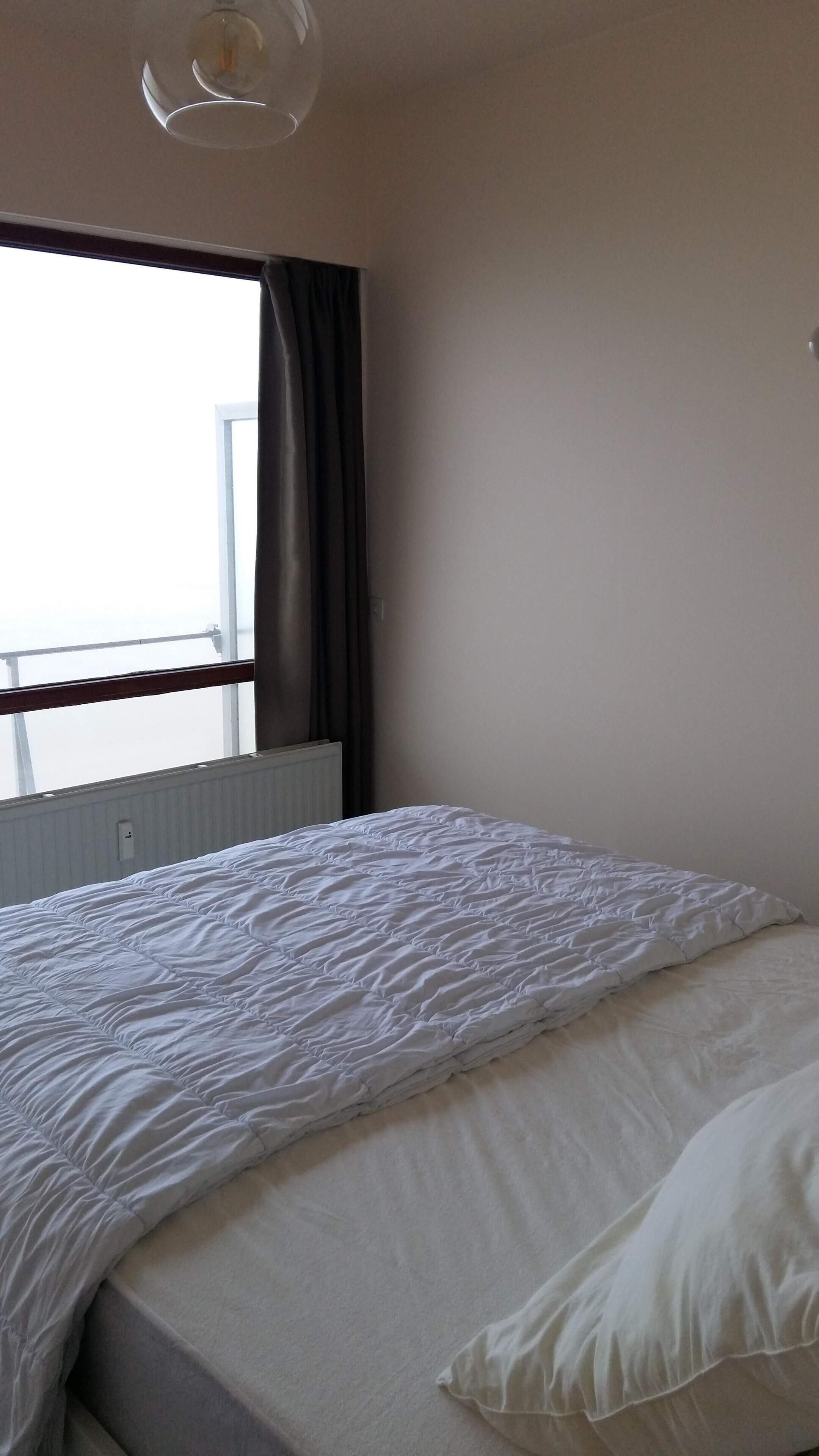 A bedroom with a bed, a window with curtains, and a radiator.