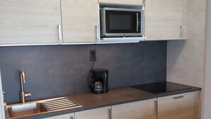 Cozinha com armários de madeira clara, bancada preta, pia de aço inoxidável e micro-ondas.