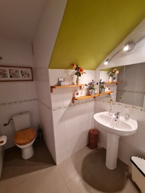Une salle de bain équipée de toilettes, d’un lavabo et d’étagères où sont rangés les articles de toilette.