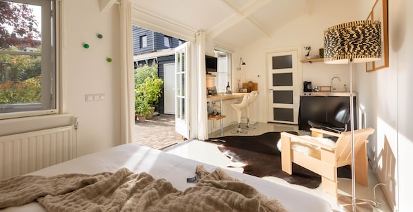 A bedroom with a bed, a desk, a chair, a TV, and a window.