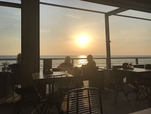 Ein Sitzbereich im Freien mit Tischen und Stühlen, der zum Meer hin ausgerichtet ist, bei Sonnenuntergang.