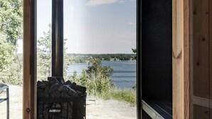 A Harvia wood stove in a room with a large window overlooking a lake and forest. - Exclusive architectural house in archipelago (Stockholm)