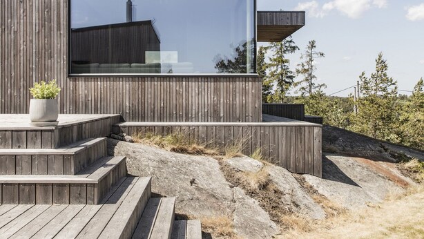 A modern wooden building with a large glass window and a wooden deck. - Exclusive architectural house in archipelago (Stockholm)